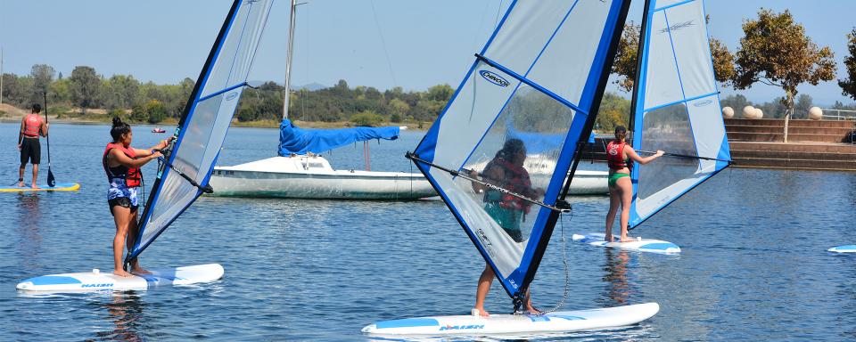 Three women on windsurf boards and a man on a stand up paddle board on Lake Natoma